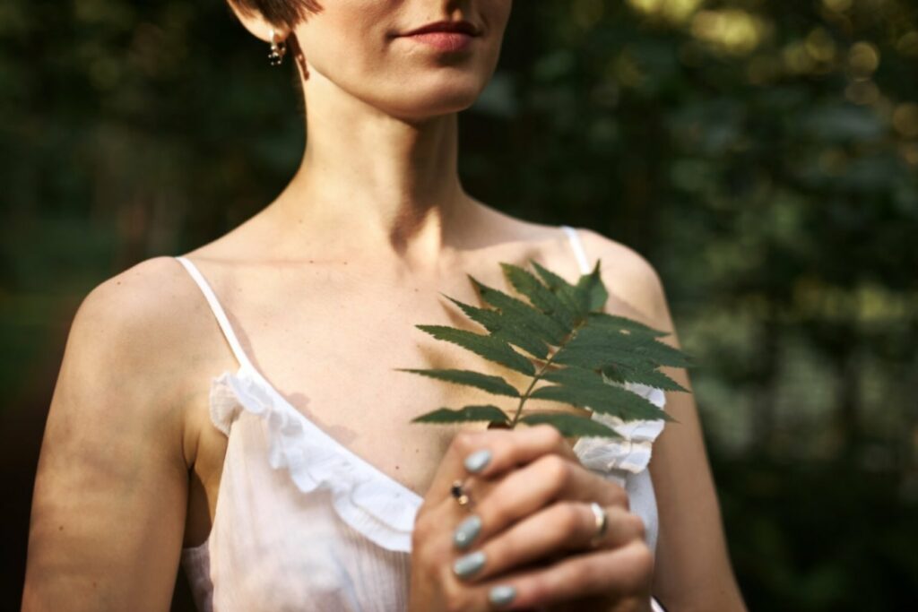 Femme sereine et épanouie, tenant une feuille d'arbre dans ses mains. Cela symbolise la paix intérieure et l'importance d'un accompagnement post-partum.