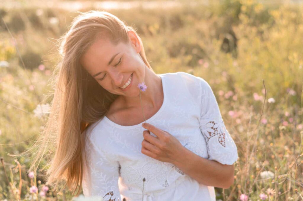 Femme souriante et épanouie tenant une fleur dans ses mains, symbolisant l'équilibre et le bien-être grâce à l'allaitement et à la contraception naturelle.