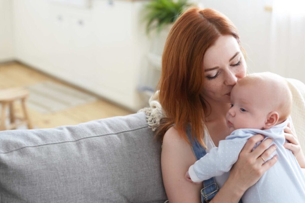 Femme portant son bébé et lui faisant un tendre bisou, illustrant un moment d'amour maternel, en lien avec l'allaitement et la contraception naturelle.