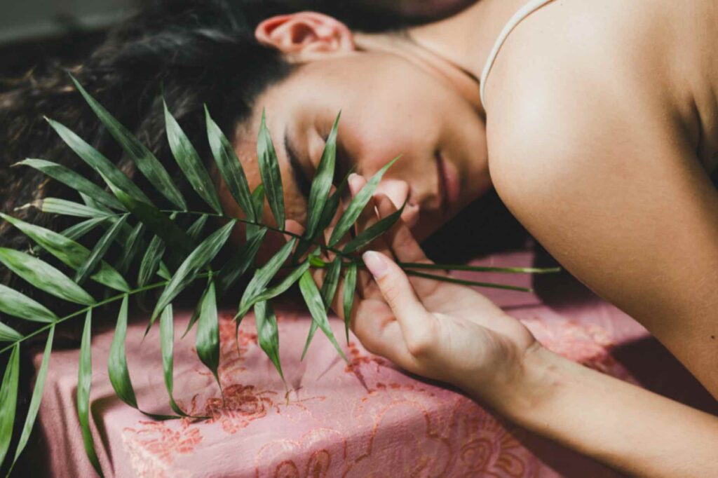 Femme endormie tenant une feuille d'arbre dans sa main, symbolisant la gestion du stress et les techniques de relaxation apportées par une naturopathe pour les problèmes gynécologiques.