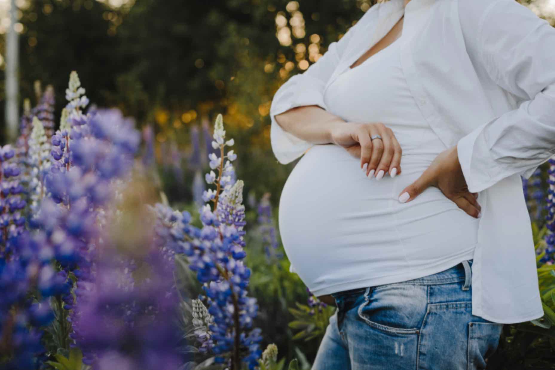 Femme enceinte, entourée de fleurs, avec son bras posé sur son ventre. Cela illustre une alimentation grossesse sereine.