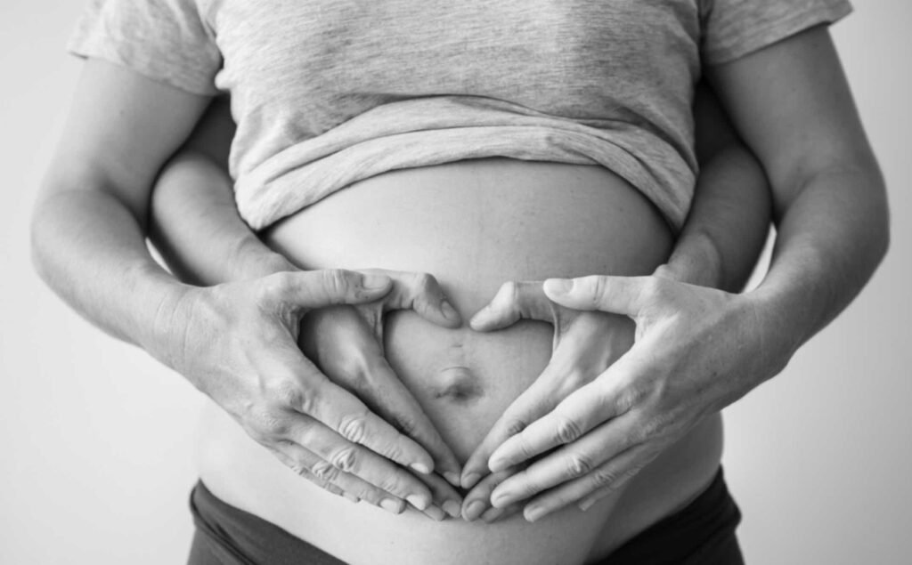Mains formant un coeur sur le ventre d'une femme enceinte, représentant l'amour et l'importance d'une alimentation grossesse sereine.